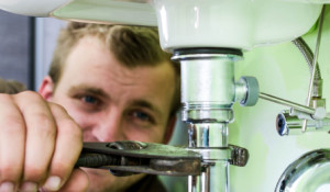 Plumber at work under a sink using a wrench