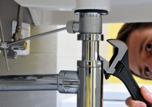 A plumber unclogging a drain pipe under a sink